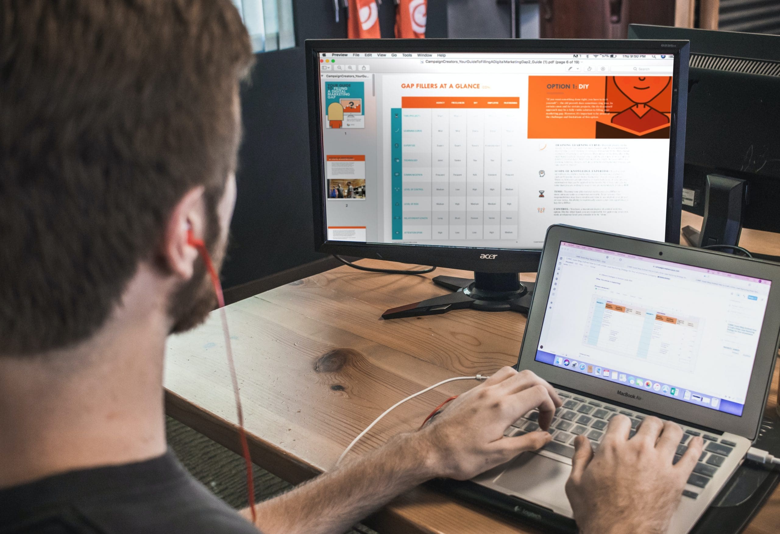 Une personne portant des écouteurs est assise à un bureau en bois ; elle travaille sur un ordinateur portable tout en consultant un graphique affiché sur un grand écran externe. Les deux écrans affichent un contenu similaire, avec des graphiques orange et blancs.