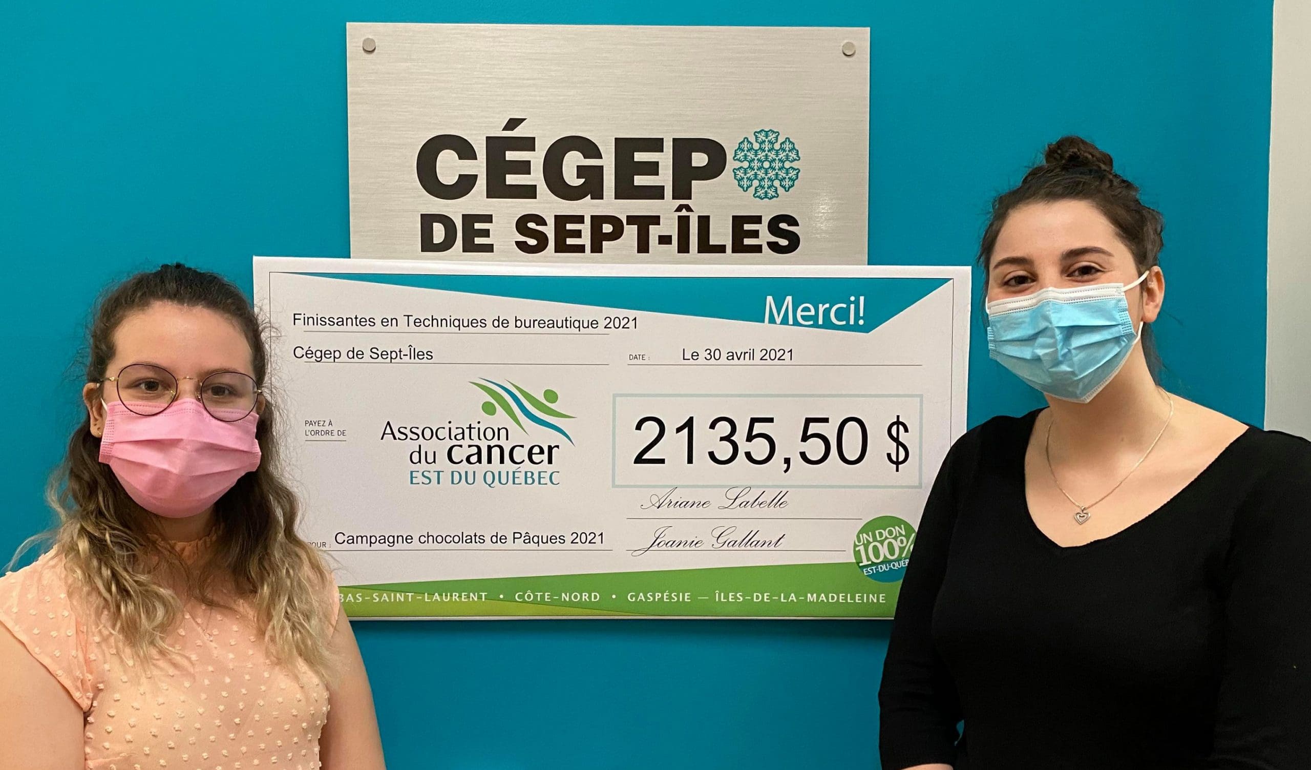 Deux femmes portant des masques se tiennent devant l'enseigne du Cégep de Sept-Îles, tenant un gros chèque d'un montant de 2 135,50 $ libellé à l'ordre de l'Association du Cancer de l'Est du Québec.