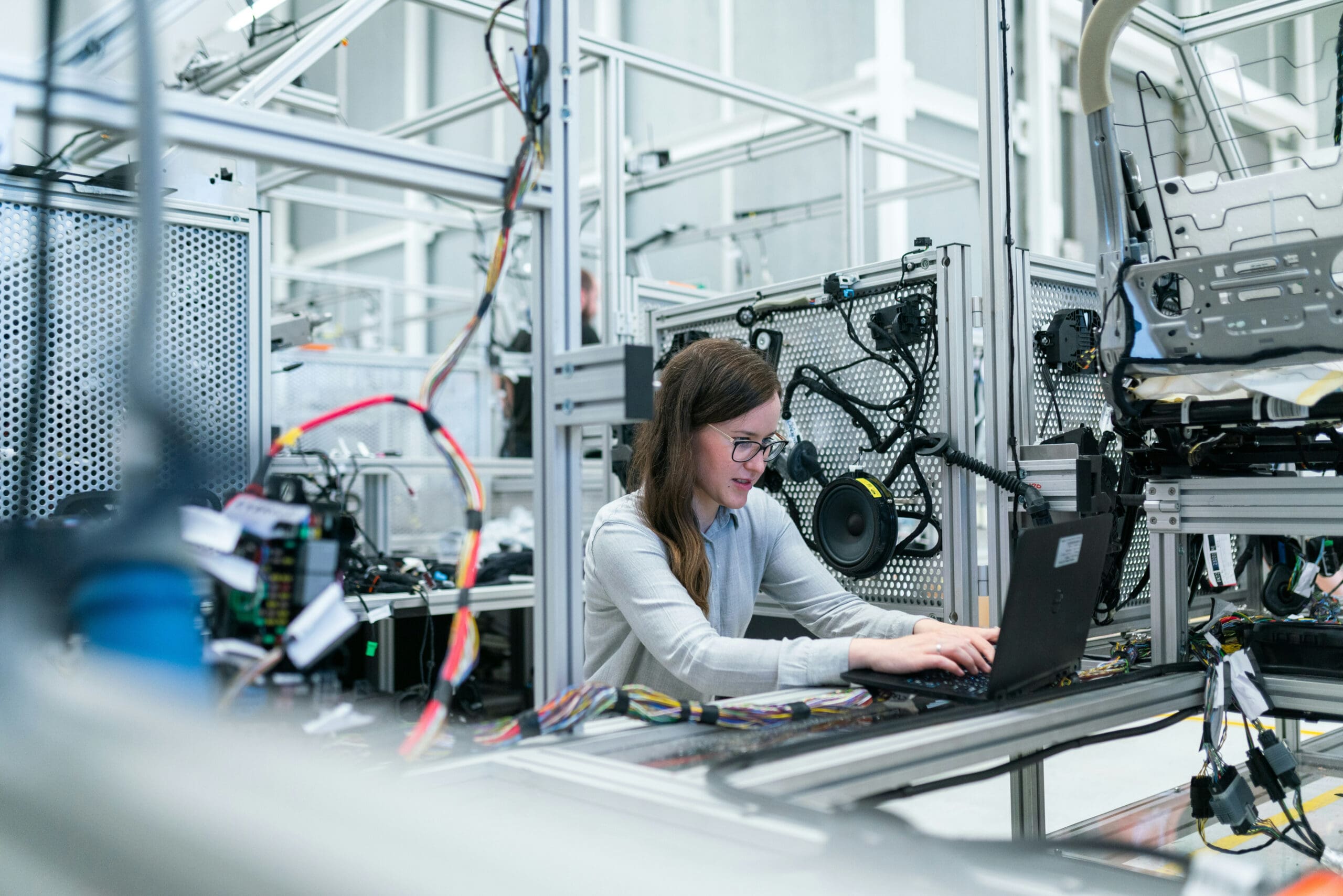 Une femme travaille sur un ordinateur portable dans un laboratoire moderne rempli de câbles, d'équipements et de machines, ce qui suggère un environnement de haute technologie ou d'ingénierie.