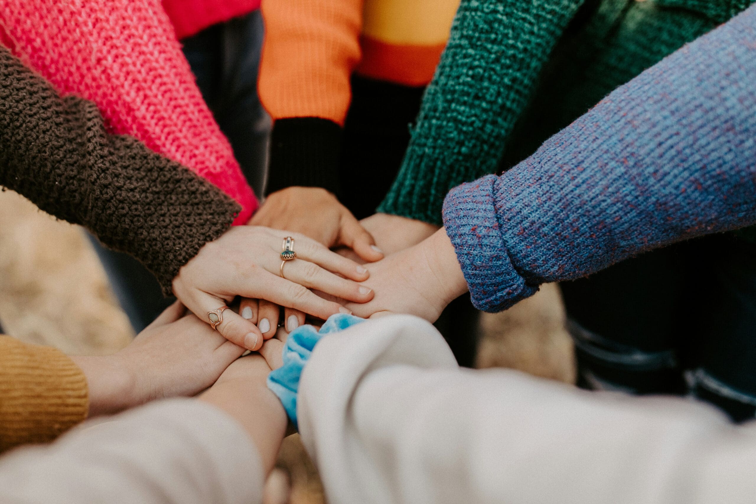 Un groupe de personnes vêtues de pulls colorés se tiennent par la main au centre, formant un cercle en signe d'unité et de travail d'équipe.
