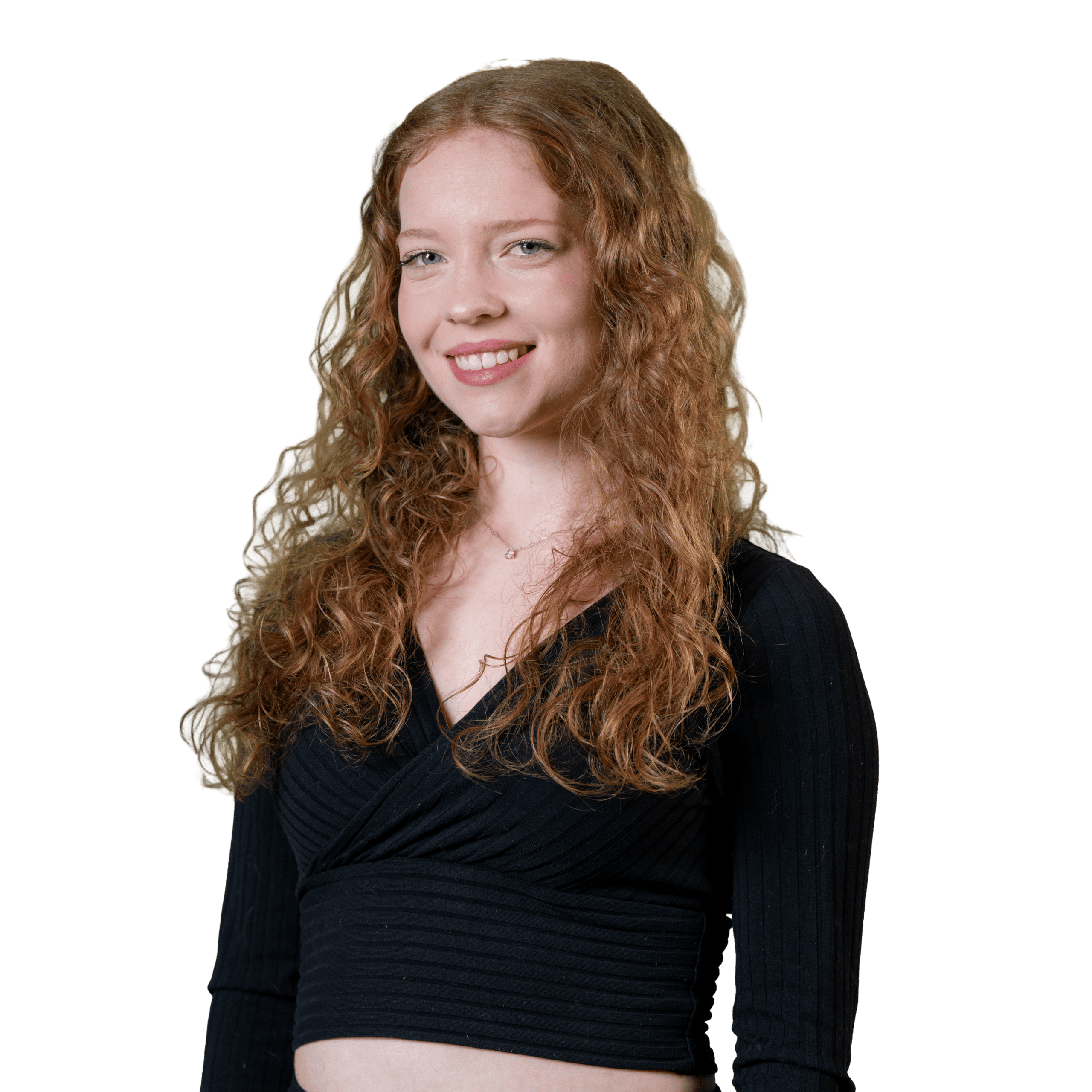 Jeune femme aux longs cheveux roux bouclés, vêtue d'un haut court noir à manches longues, souriante, debout devant un fond blanc uni.