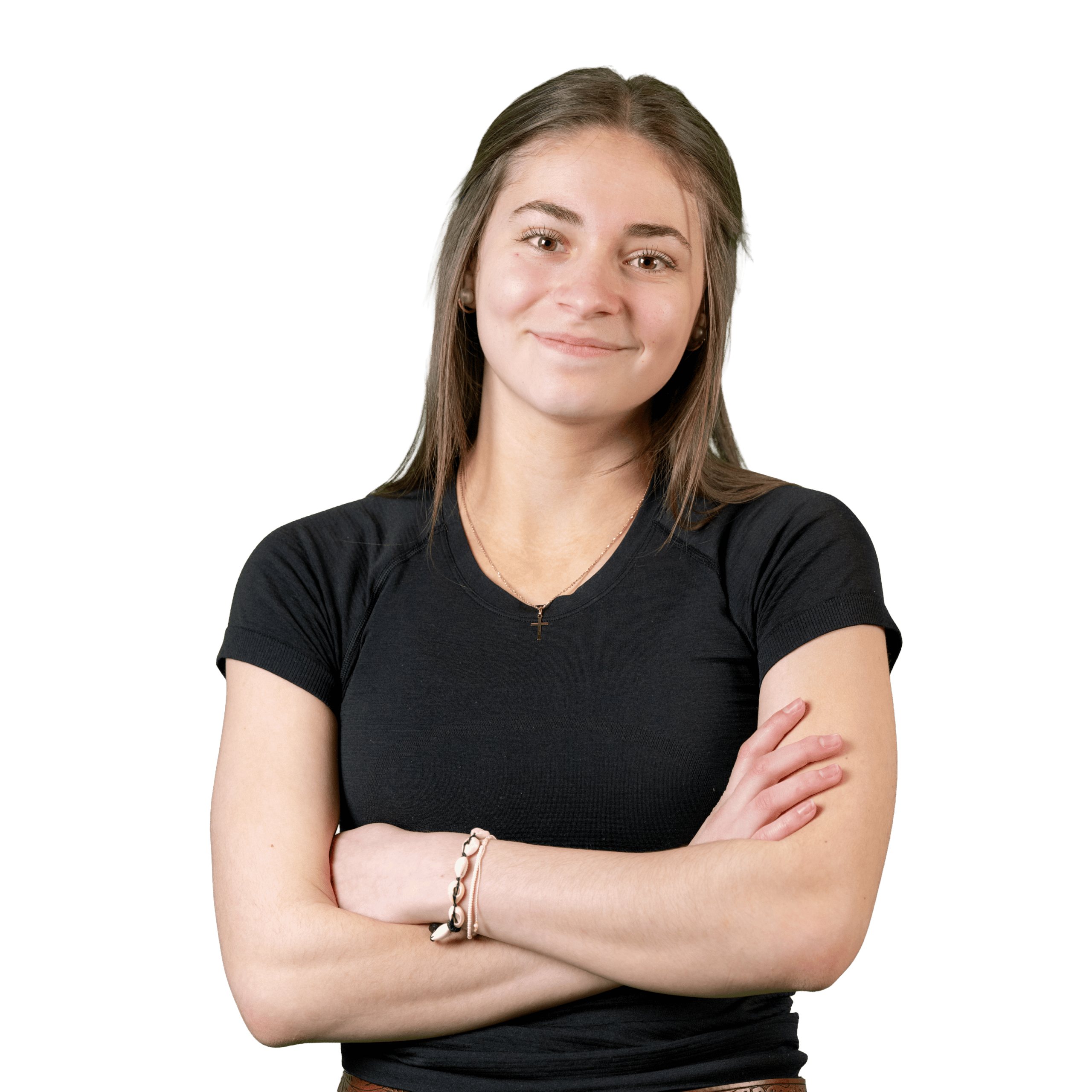 Une jeune femme aux cheveux bruns et raides se tient debout devant un fond blanc, les bras croisés, et sourit doucement. Elle porte un t-shirt noir à manches courtes, un collier et des bracelets au poignet gauche.