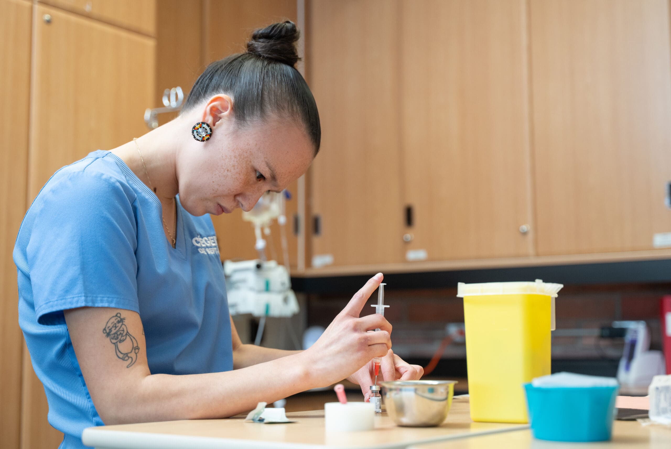 Une personne vêtue d'une blouse bleue prépare une seringue à un bureau dans un environnement médical ou de laboratoire, entourée de récipients et de matériel médical.