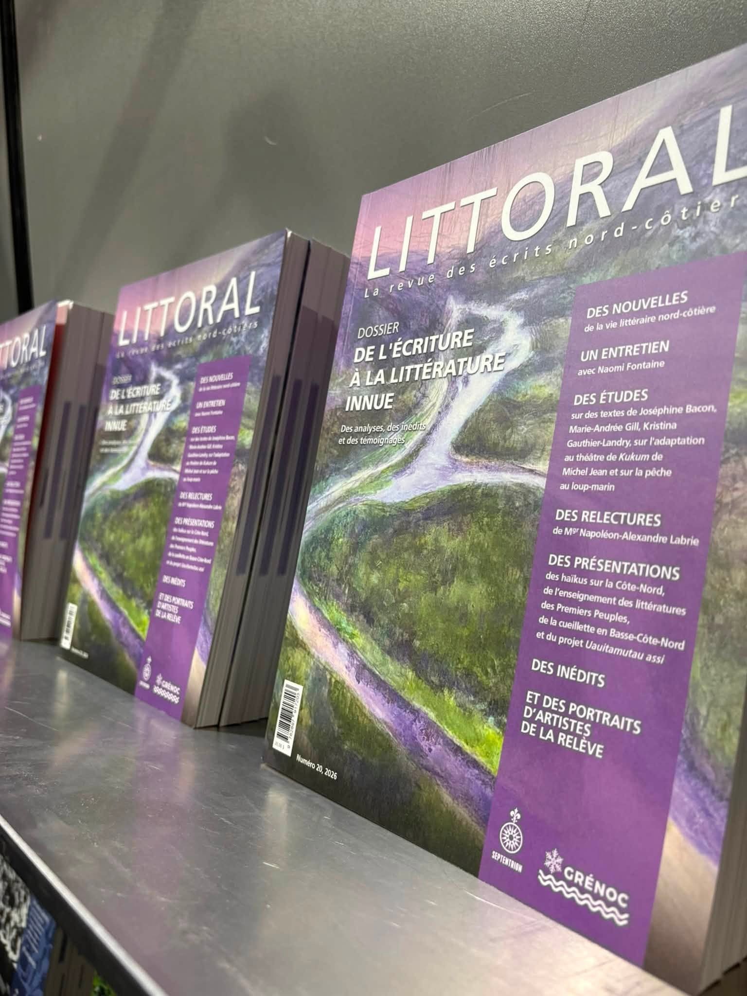 Plusieurs exemplaires du magazine « Littoral » sont disposés à la verticale sur une étagère. La couverture présente une peinture représentant un paysage aux tons violets et verts, ainsi qu'un texte en français mettant en avant des articles sur la littérature innue, des interviews et des études.