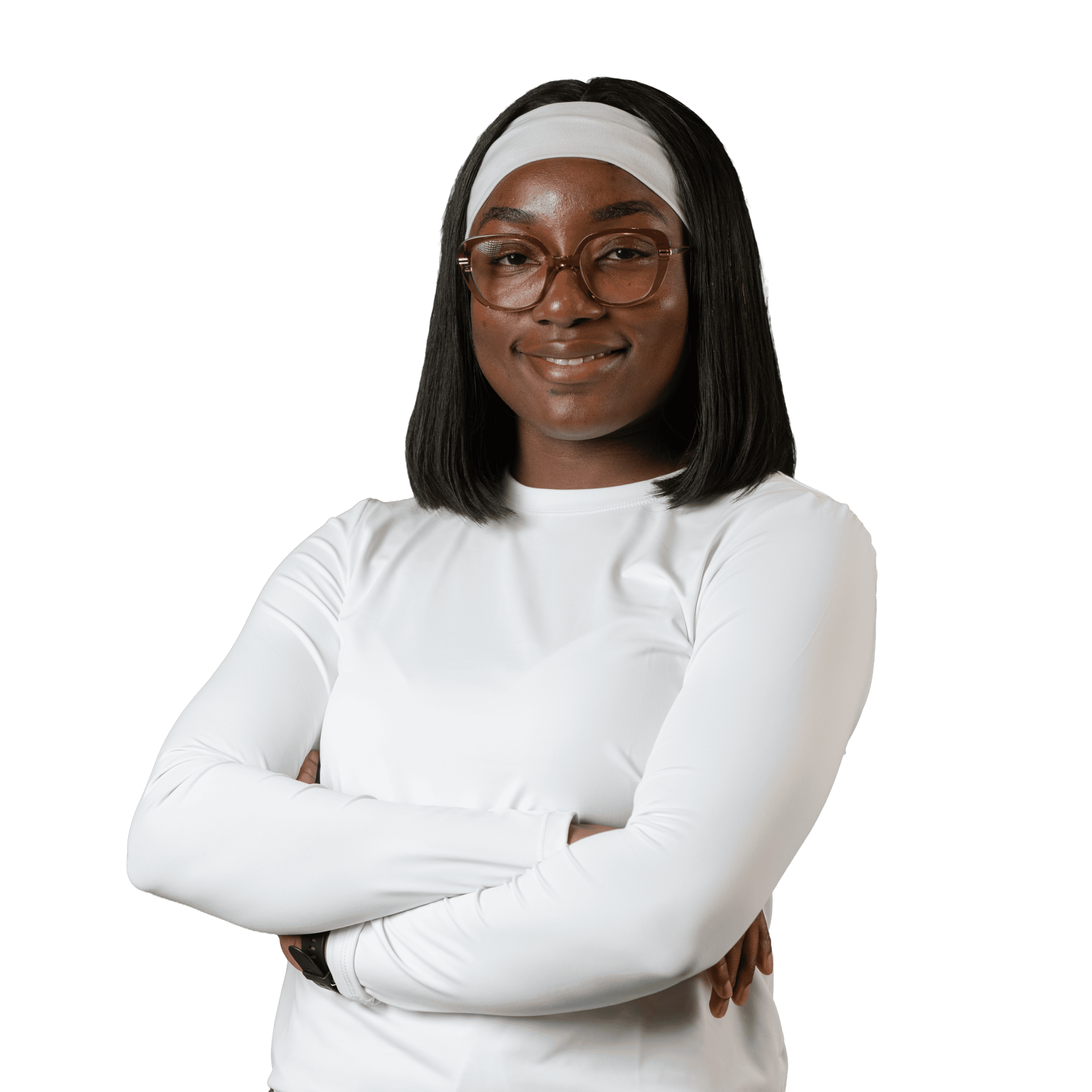 Une femme aux cheveux noirs raides, portant des lunettes, un bandeau blanc et un t-shirt blanc à manches longues, se tient debout, les bras croisés, et sourit avec assurance sur un fond blanc uni.
