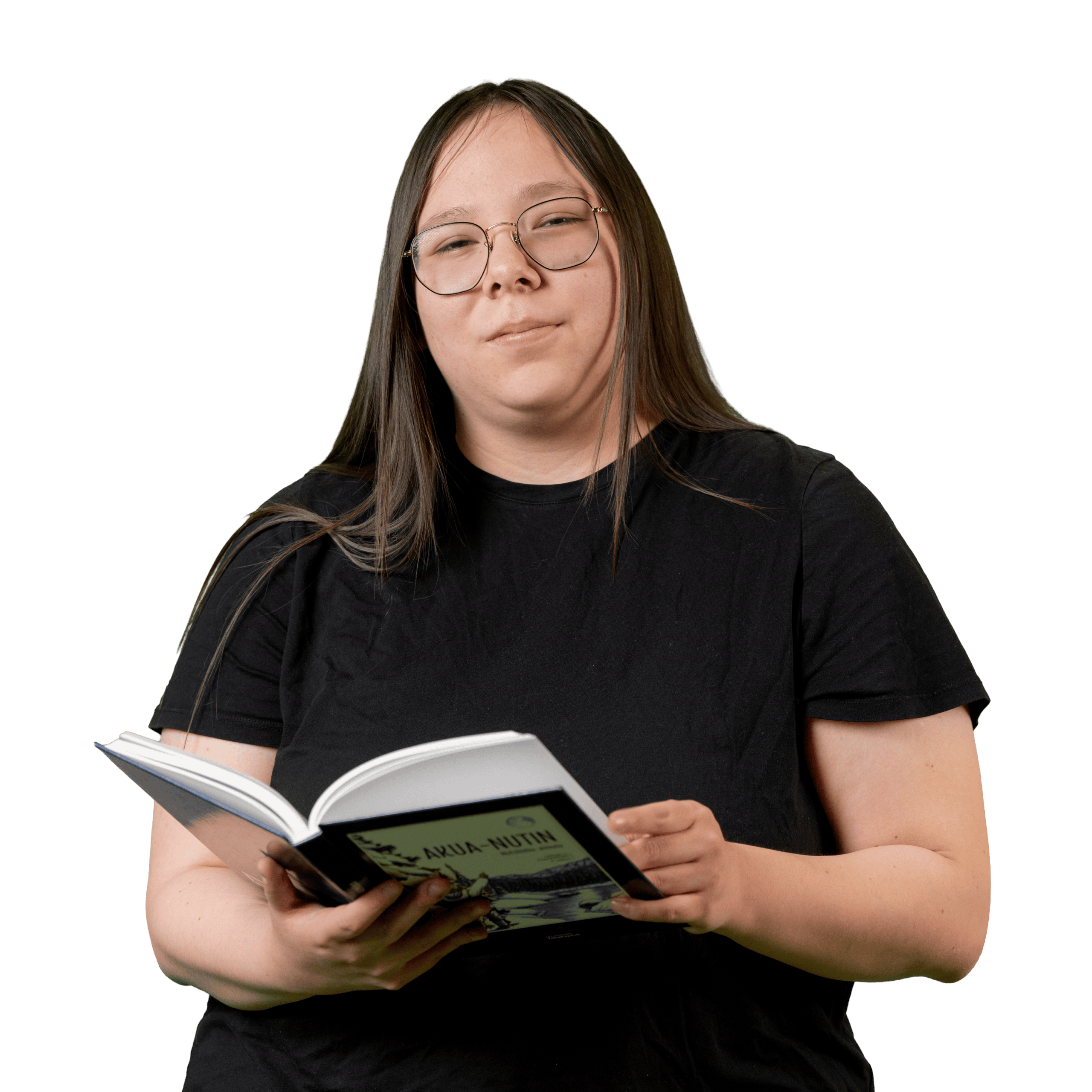 Une personne aux cheveux longs et portant des lunettes, vêtue d'un t-shirt noir, tient un livre ouvert et regarde vers l'appareil photo devant un fond blanc uni.