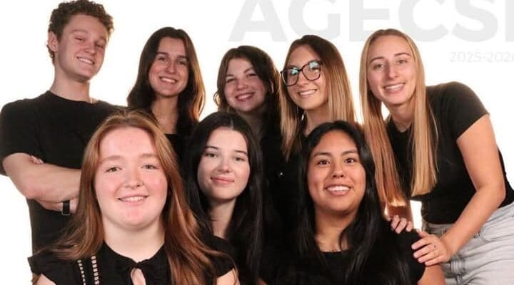 Un groupe de huit jeunes adultes, dont cinq assis à l'avant et trois debout à l'arrière, tous souriants et vêtus de noir, posent ensemble devant un fond blanc.